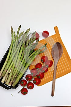 Fresh cherry tomatoes and green raw asparagus on white background with copy space. Vegetarian meal ingredients.