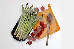 Fresh cherry tomatoes and green raw asparagus on white background with copy space. Vegetarian meal ingredients.