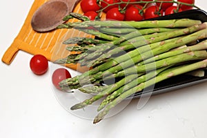 Fresh cherry tomatoes and green raw asparagus on white background with copy space. Vegetarian meal ingredients.