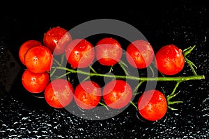 Fresh cherry tomatoes on the vine on black background with water puddles