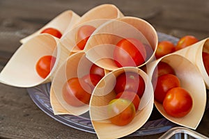 Fresh cherry tomatoes in wooden cones on a purple plate, ideal for organic food markets...Fresh cherry tomatoes in wooden cones on