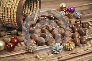 Fresh chestnuts in the basket falling on a brown wooden table, along with christmas decorations