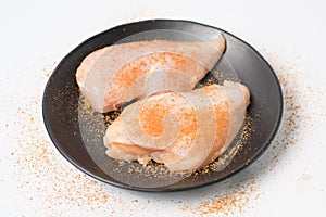 Fresh chicken breast fillets seasoned with spices on black dish