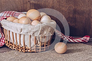 Fresh chicken eggs in a basket on a wooden table. Canvas napkin on the table.