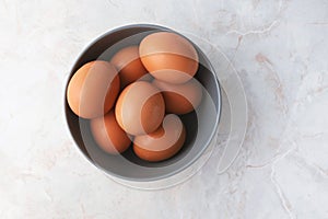 Fresh chicken eggs in gray bowl on white marble table background. Farm products, natural eggs