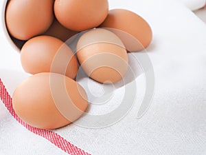 Fresh chicken eggs in a white bucket  on a white dishcloth with red straight stripes.