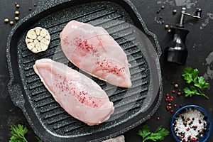 Fresh chicken meat with spices on a grill pan, black stone grunge background. Raw chicken fillet. Top view, flat lay.
