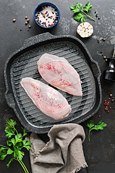 Fresh chicken meat with spices on a grill pan, black stone grunge background. Raw chicken fillet. Top view, flat lay.