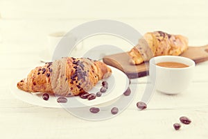 Fresh chocolate croissants and cup of coffee on white rustic woo