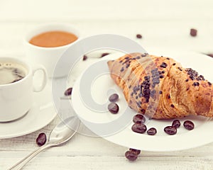 Fresh chocolate croissants and cup of coffee on white rustic woo