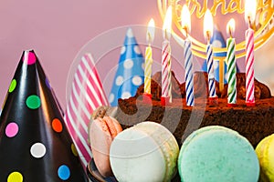 Fresh cholocate delicious cake with maracoons around it with topper Happy birthday and burning candles on the table