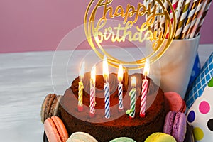 Fresh cholocate delicious cake with maracoons around it with topper Happy birthday and burning candles on the table