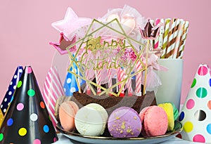 Fresh cholocate delicious cake with maracoons around it with topper Happy birthday on the table against pink background.