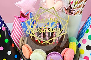 Fresh cholocate delicious cake with maracoons around it with topper Happy birthday on the table against pink background.