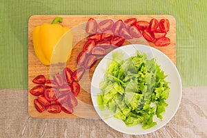 Fresh chopped green lettuce leaves lie on a wooden cutting board next to the yellow bell pepper and chopped red cherry