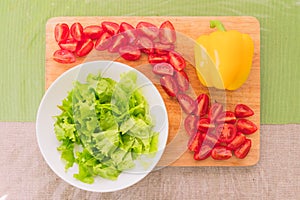 Fresh chopped green lettuce leaves lie on a wooden cutting board next to the yellow bell pepper and chopped red cherry