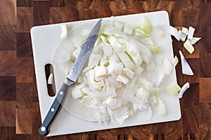 Fresh chopped onion on white cutting board with knife, on wood butcher block