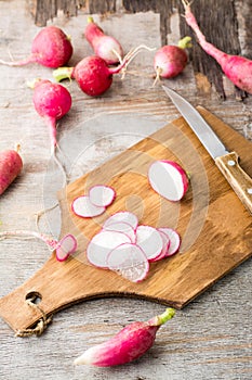 Fresh chopped radishes and a knife on a cutting board on a wooden table. Vegetables for a vegetarian diet. Rustic style.