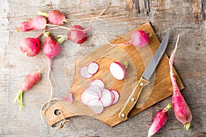 Fresh chopped radishes and a knife on a cutting board on a wooden table. Vegetables for a vegetarian diet. Rustic style. Top view