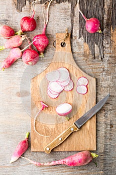 Fresh chopped radishes and a knife on a cutting board on a wooden table. Vegetables for a vegetarian diet. Rustic style. Vertical