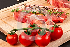 Chopped raw pork steaks with seasoning, ripe tomatoes and thyme on a cutting kitchen board on a black wooden table