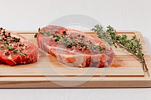 Chopped raw pork steaks with spices and thyme on a cutting kitchen board on a white wooden table