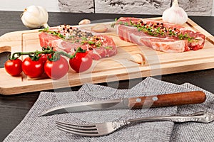 Chopped raw pork steaks with spices, tomatoes and thyme on a cutting kitchen board on a black wooden table. next to a napkin with