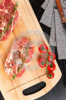 fresh chopped raw pork steaks with spices, tomatoes and thyme on a cutting kitchen board on a black wooden table