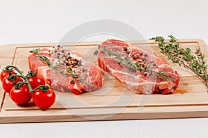 Fresh chopped raw pork steaks with spices, tomatoes and thyme on a cutting kitchen board on a white table