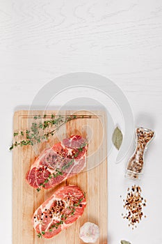 Fresh chopped raw steaks with spices and thyme on a cutting kitchen board on a white wooden table