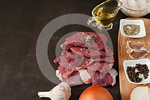 Fresh chunks of raw beef, onions, garlic, olive oil and spices are close-up ready to cook on a dark background