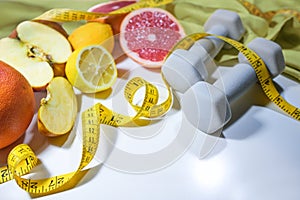 Fresh citrus fruits, apples, measuring tape and dumbbells, concept for a healthy lifestyle with fitness, sports and vitamin rich