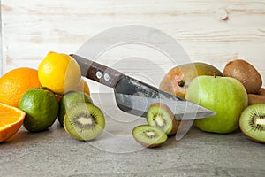 Fresh citrus fruits, half cut kiwi orange and lemons on cutting board with knife on stone background.
