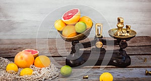 Fresh citrus fruits on the one scalepan of vintage weights and and few oranges, lemons, grapefruit, lime on the rustic wooden
