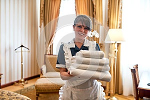 Fresh and clean. Hotel maid in uniform smiling while holding stack of clean white towels for guests while cleaning and
