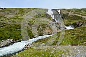 Fresh clean small waterfall in Iceland in summer with loads of water flowing between rocks, snow in the