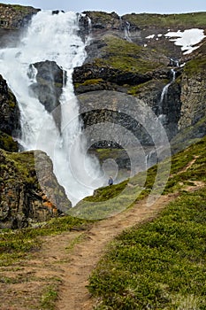 Fresh clean small waterfall in Iceland in summer with loads of water flowing between rocks and unrecognisable person by the