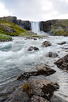 Fresh clean waterfall Gufufoss near Seydisfjordur in Iceland in summer with loads of water flowing between rocks, snow in the