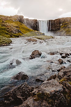 Fresh clean waterfall Gufufoss near Seydisfjordur in Iceland in summer with loads of water flowing between rocks, snow in the