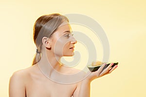 Fresh. Close up of beautiful female face with half avocado over yellow background. Cosmetics and makeup, natural and eco