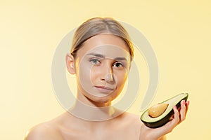 Fresh. Close up of beautiful female face with half avocado over yellow background. Cosmetics and makeup, natural and eco