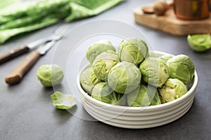 Fresh, close up brussels sprouts in white plate isolated on dark background. Healthy vegan food, diet concept