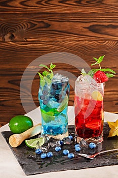 Fresh cocktails with mint, lime, ice, berries and carambola on the wooden background. Refreshing summer beverages. Copy space.