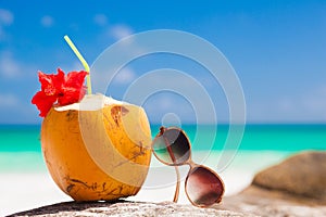 Fresh coconut cocktail decorated with hibiscus flower and sunglasses on a tropical beach