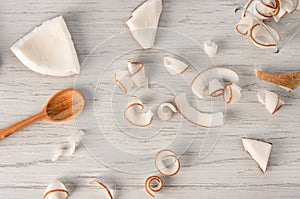 Fresh coconut flesh slices and spirals with wooden spoon and circles on white table, flat lay