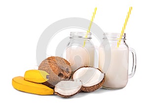 Fresh coconuts, two tasty, bright yellow bananas and two mason jar full of natural coconut milk isolated on a white background