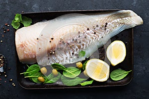 Fresh cod fillet of white sea fish before cooking with sea salt, olive oil, herbs and pepper. Healthy eating concept