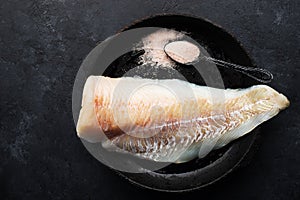 Fresh cod fillet of white sea fish before cooking with sea salt, olive oil, herbs and pepper. Healthy eating concept