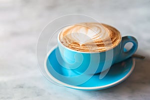 Fresh coffee with heart love foam in blue cup marble background