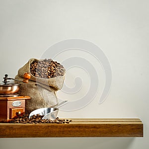 Fresh coffee in jute sack on wooden shelf with empty copy space for your products and decoration. Light gray wall background.